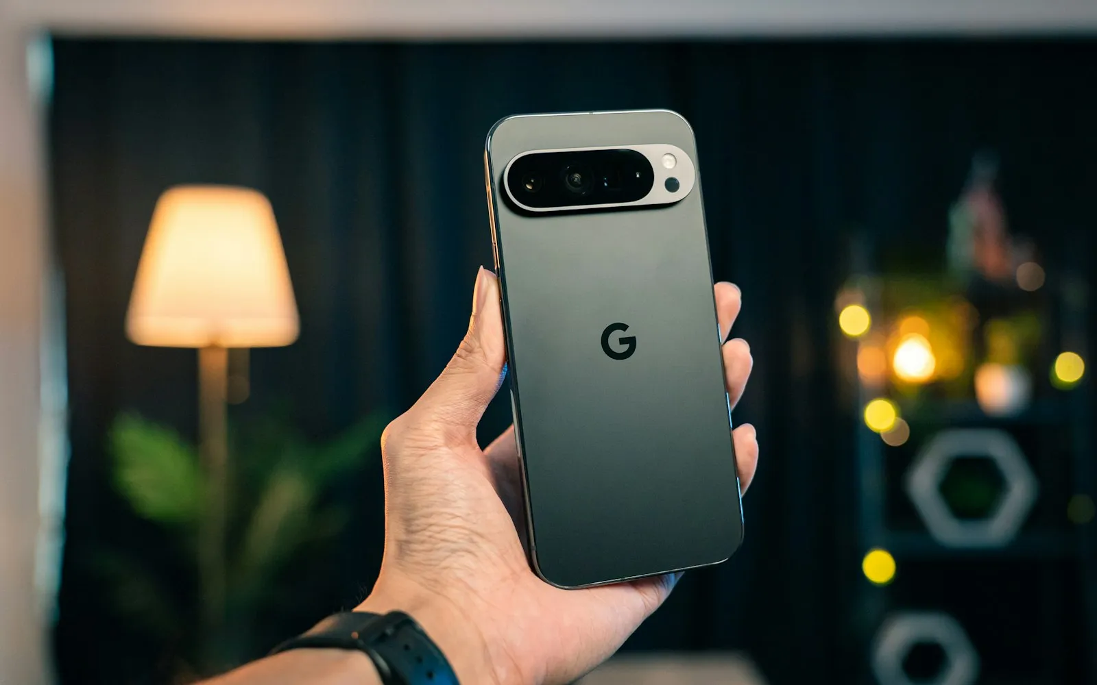 A hand holding a grey Android smartphone with a horizontal camera bar in a softly lit room