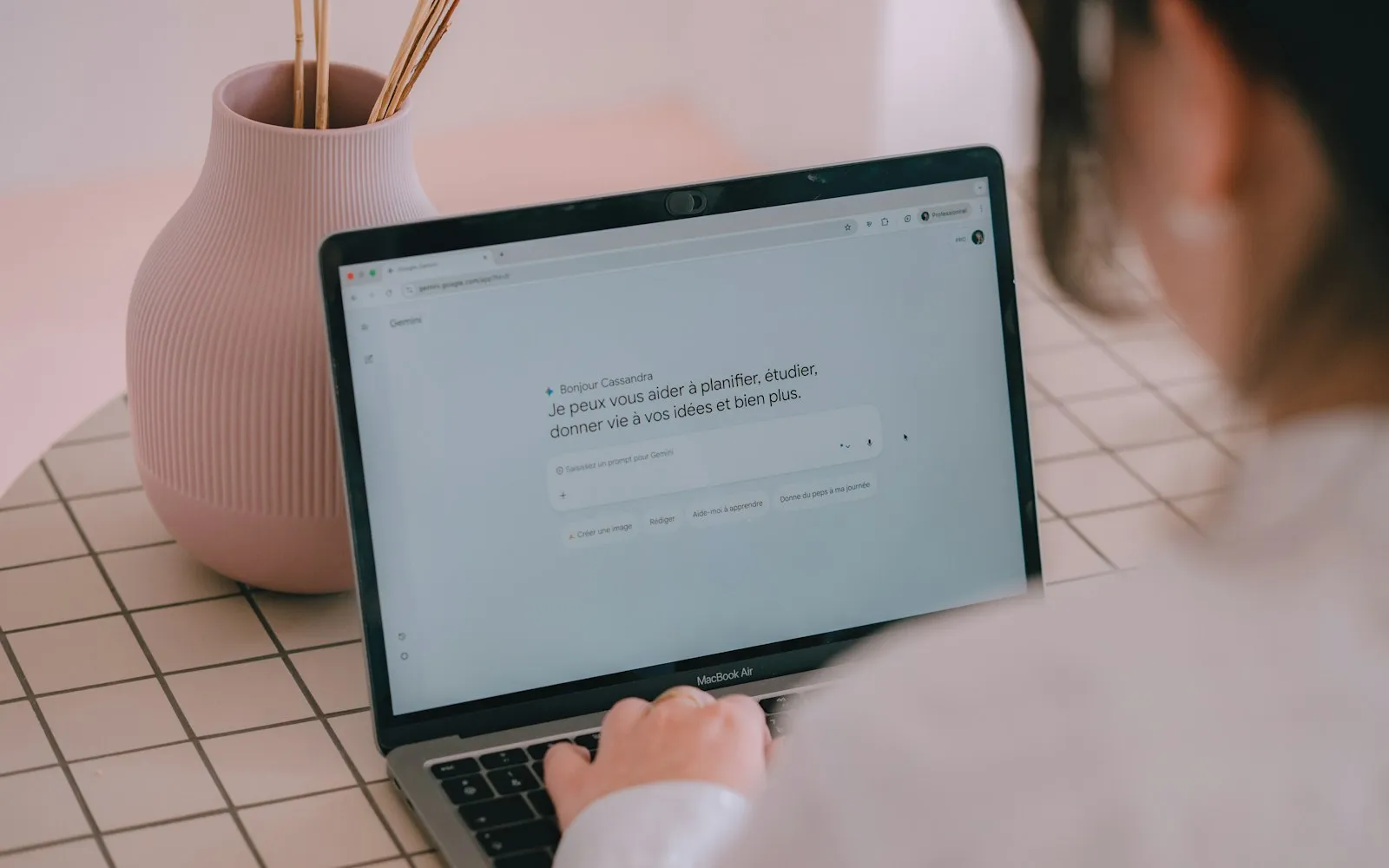 A person typing on a laptop at a table with a pink vase and a checked tablecloth
